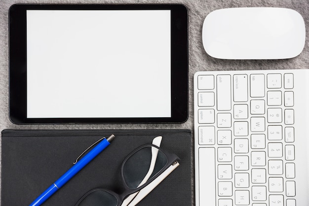 Close-up of office desk with digital tablet; mouse; keyboard; pen; eyeglasses and diary on desk