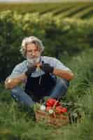 Free photo close up of old farmer holding a basket of vegetables. the man is standing in the garden. senior in a black apron.