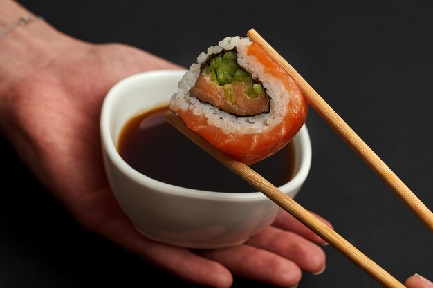 Крупный план суши-ролла с лососем и огурцом в соевом соусе. выборочный фокус. темный фон