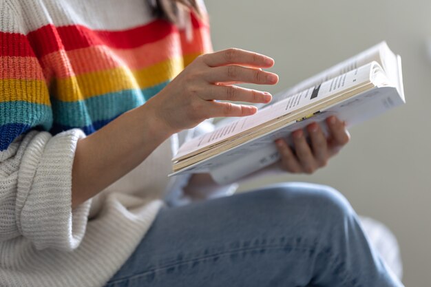 Primo piano di un libro aperto nelle mani di una ragazza in un maglione colorato brillante.