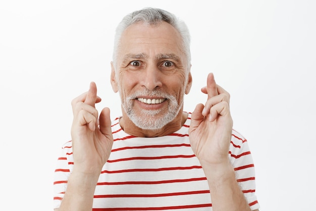 Close-up of optimistic hopeful senior man, cross finger good luck, making wish