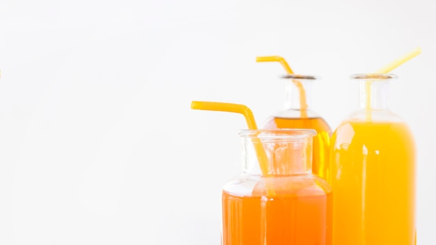 Close-up of an oranges and mango juice bottles with drinking straws isolated on white background