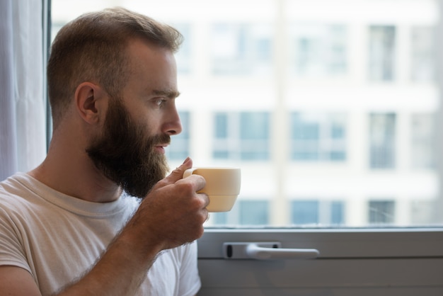 Primo piano di uomo pensoso hipster bere caffè dalla tazza