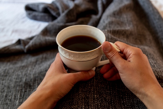 一杯のコーヒーを保持しているベッドでクローズアップ人