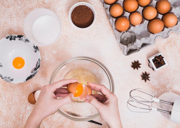 Close-up of a person breaking the eggs in the glass bowl for making the cake dough