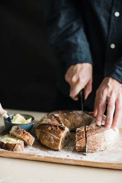 Close-up of a person cutting bagel with knife on chopping board