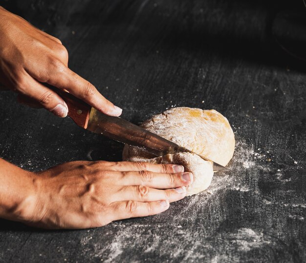 Close-up person cutting dough on black table