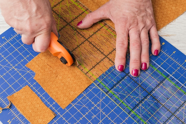Close Up Of A Person Cutting Fabric Pieces By Rotary Cutter On Mat