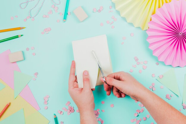 Close-up of a person cutting the paper with scissor on teal backdrop