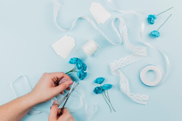 Close-up of a person cutting the ribbon with scissor for tying the blue roses on colored backdrop