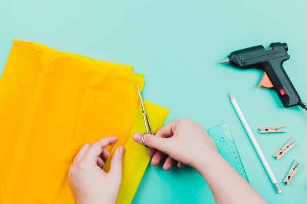 Close-up of a person cutting the yellow paper with scissor on turquoise backdrop