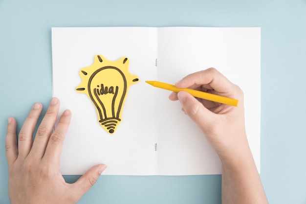 Close-up of person drawing light bulb on white page over the gray background