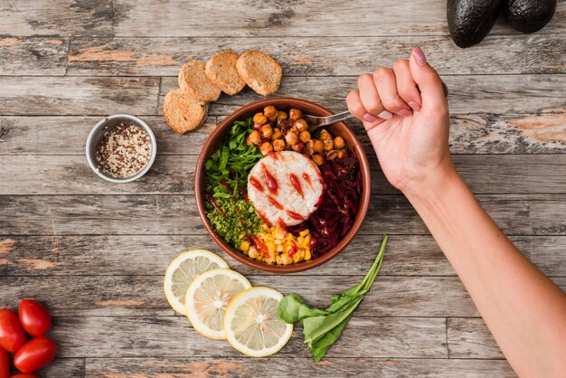 Close-up of a person eating the burrito bowl with bread and lime slices on wooden desk