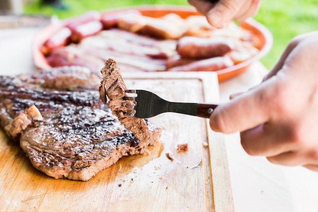 Close-up of a person eating steak on chopping board with fork and knife