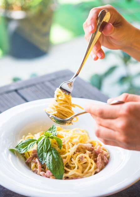 Close-up of a person holding appetizing spaghetti rolled on fork in the spoon