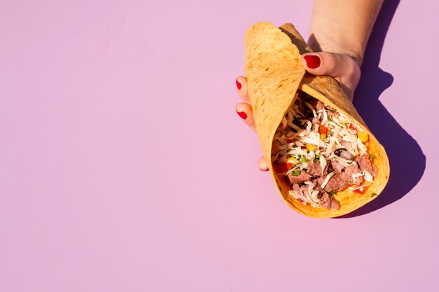 Close-up person holding burrito with purple background