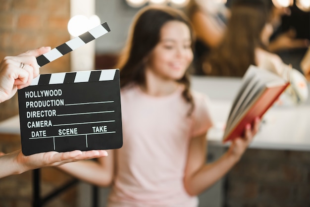 Close-up of a person holding clapper board in front of girl rehearsing