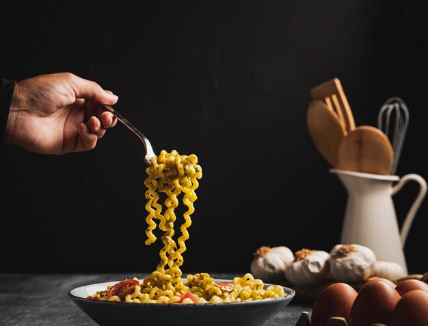 Close-up person holding curly pasta with fork