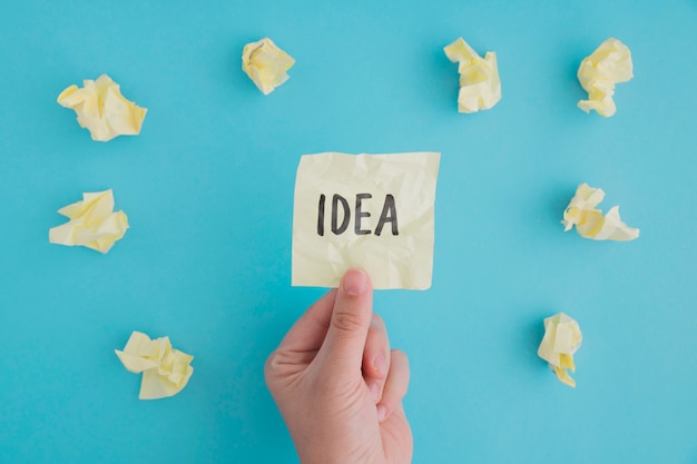 Close-up of a person holding idea paper with crumpled ball of papers on blue backdrop