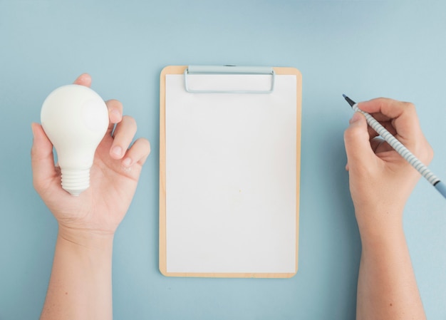 Close-up of a person holding light bulb writing with felt pen on clipboard