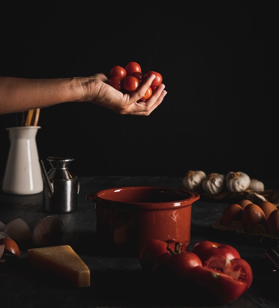 Close-up person holding tomatoes with dark background 