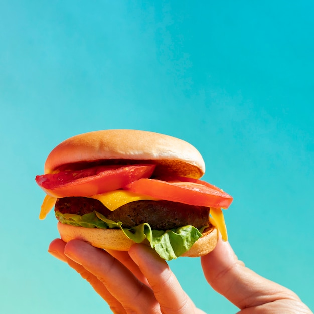 Close-up person holding up cheeseburger