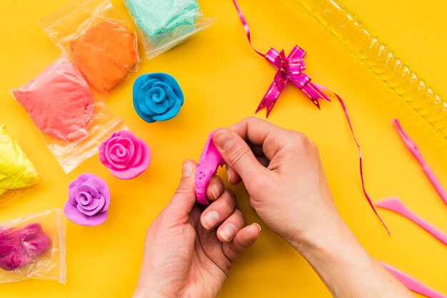 Close-up of a person making colorful clay rose on yellow backdrop