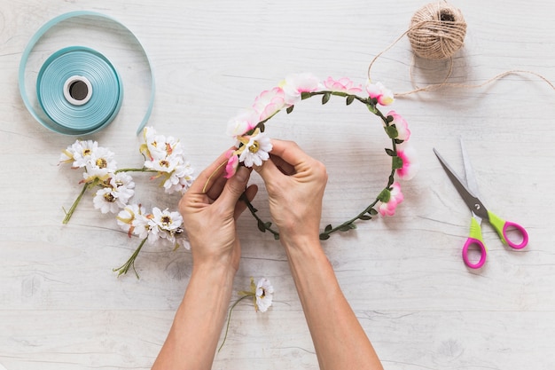 Close-up of a person making decorating flower wreath over white textured background