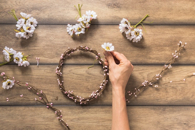 Close-up of person making flower and twig wreath on wooden table