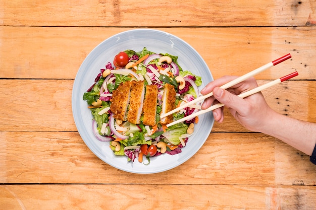 Close-up of a person picking thai food with chopsticks on wooden desk