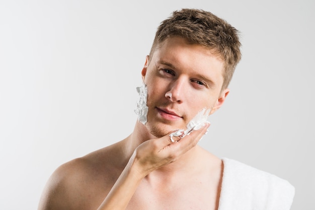 Free photo close-up of a person's hand applying shaving foam on his cheek isolated on grey background