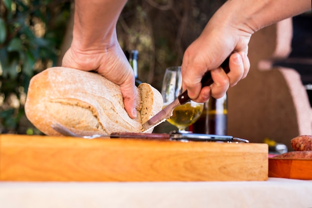 Close-up of a person's hand cutting loaf of bread on chopping board