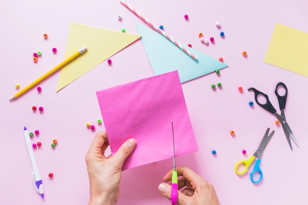 Free photo close-up of a person's hand cutting paper over the pink background