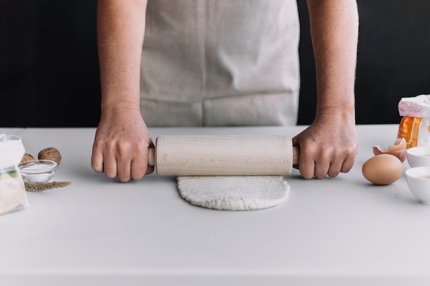 Close-up of a person's hand flattening dough with rolling pin on kitchen counter