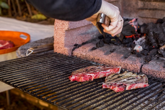 Close-up of a person's hand grilling beef rib in bbq