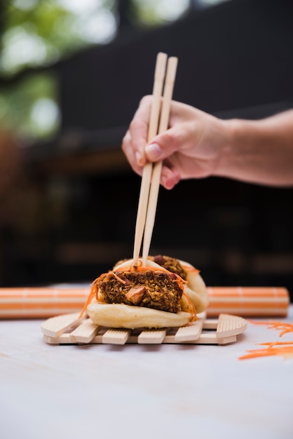 Крупный план руки человека, держащего палочки для еды над вареным вареником с мясной и овощной начинкой