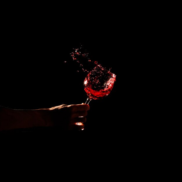 Close-up of a person's hand holding glass of red wine splashing out of glass