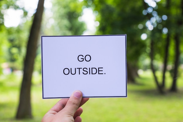 Close-up of a person's hand holding placard with go outside text