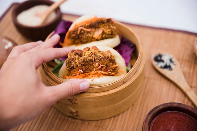 Close-up of a person's hand holding taiwan's traditional food gua bao in steamer
