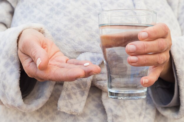 Крупный план руки человека, держащего белую таблетку и стакан воды