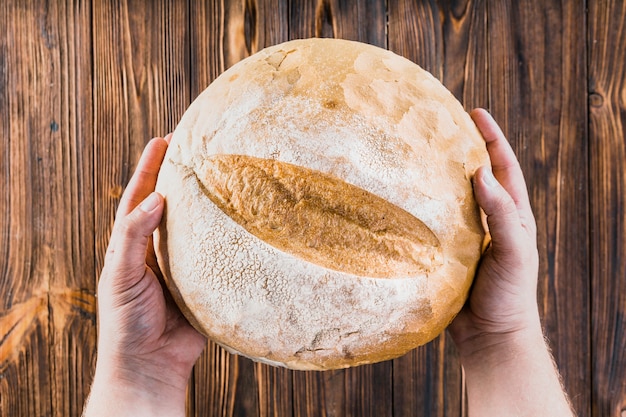 Close-up of a person's hand holding whole loaf of bread