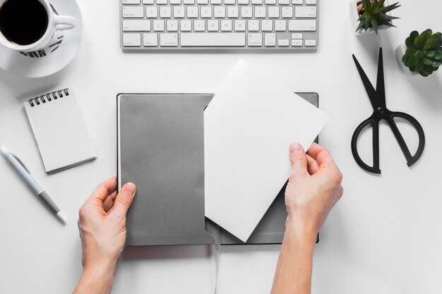 Close-up of a person's hand inserting blank white paper in the gray cover on workspace desk