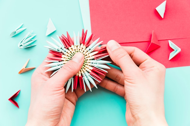 Close-up of a person's hand making the paper flower on teal background