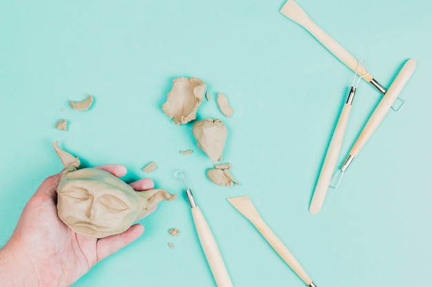 Close-up of a person's hand preparing the alien face with clay using sculpting tools on mint green background