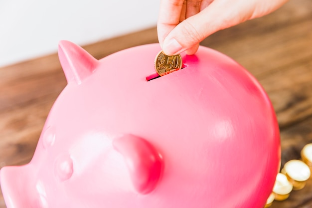 Close-up of a person's hand saving coin in pink piggybank