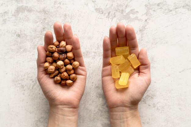 Close-up of person's hand showing hazelnut and candy over concrete background