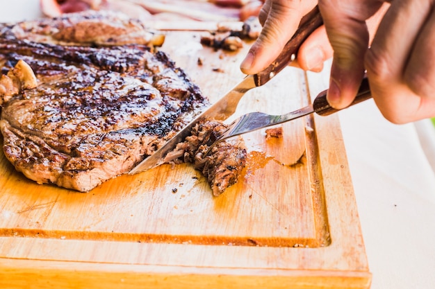Close-up of a person's hand slicing meat with fork and knife