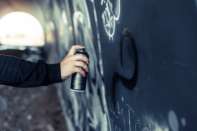 Close-up of a person's hand spraying paint with aerosol can on graffiti wall