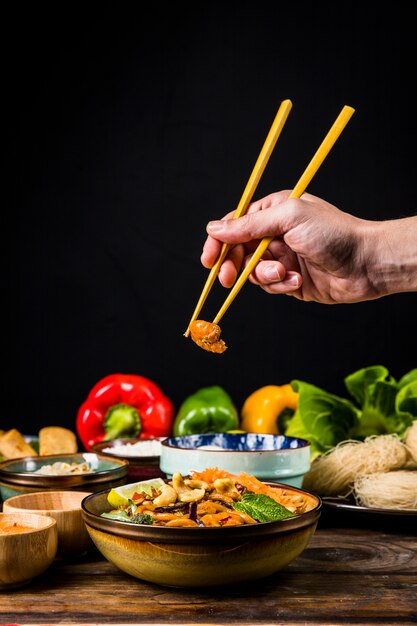 黒の背景に木製の机の上のボウルに麺からエビを取っている人の手のクローズアップ