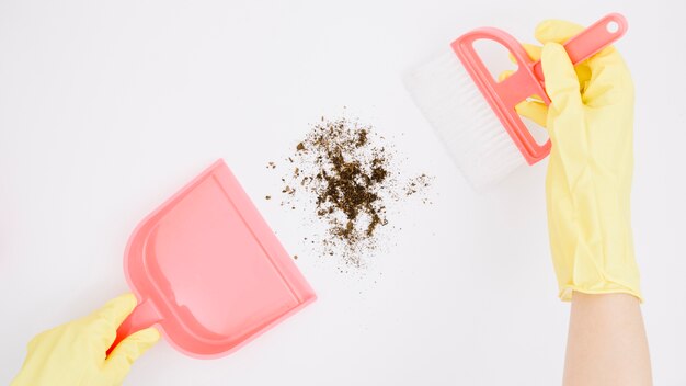 Close-up of a person's hand wearing gloves taking dust on dustpan with cleaning brush